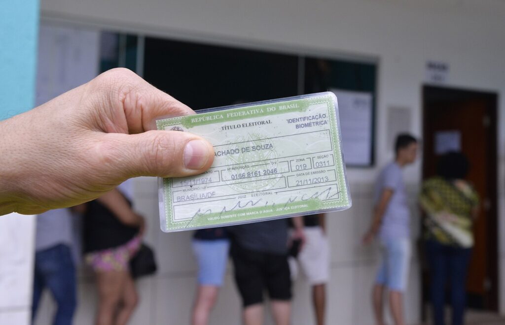 Eleitor segura o título na fila: a colinha eleitoral vai junto, no papel